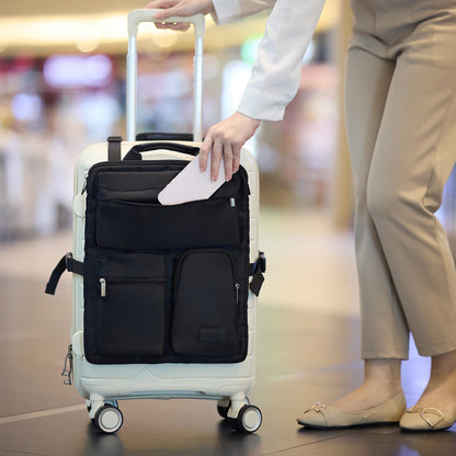 Black luggage handle hanging bag mounted over a white carry-on suitcase while a traveler slides a tablet in